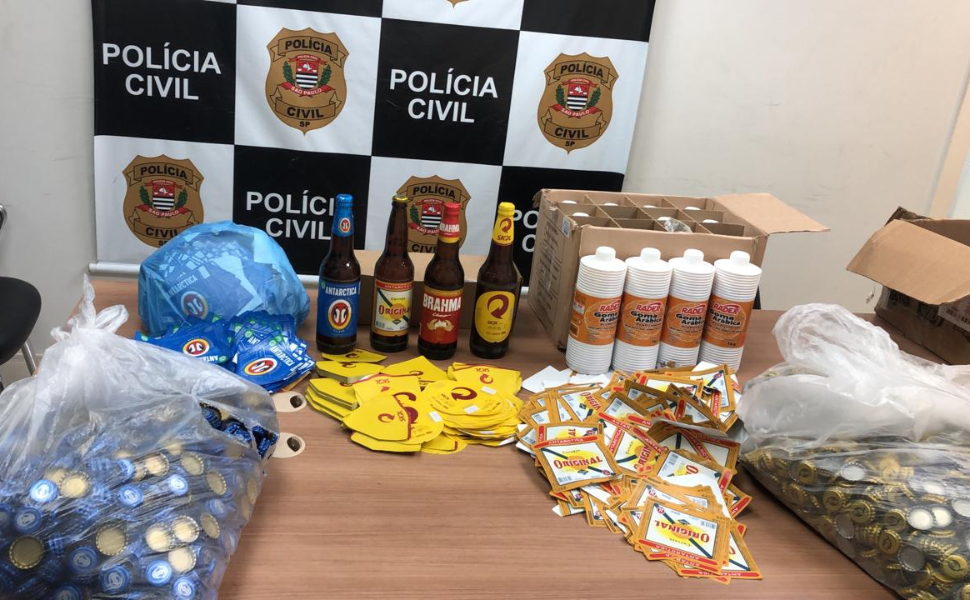 Fábrica clandestina de bebidas é descoberta em Piracicaba (Foto: Polícia Civil) Durante monitoramento discreto, os policiais constataram que os portões da propriedade estavam abertos e encontraram um caminhão estacionado. Ao se aproximarem, ouviram sons de pessoas tentando fugir, mas conseguiram deter quatro suspeitos, todos com idades entre 20 e 31 anos e naturais da capital e da Grande São Paulo. Eles foram presos em flagrante e levados à cadeia anexa ao Plantão Policial, onde permaneceram à disposição da Justiça. No interior da chácara, os agentes encontraram um salão improvisado com condições precárias de higiene e moradia, além de equipamentos utilizados para falsificação, como uma prensa mecânica, tampinhas de garrafa com logotipos de marcas conhecidas e rótulos diversos. Segundo a investigação, garrafas de cervejas populares estavam sendo reutilizadas e maquiadas com rótulos e tampas de marcas mais caras, simulando produtos originais. A perícia técnica foi acionada e compareceu ao local para analisar o material. Entre os itens apreendidos estavam um caminhão Mercedes-Benz (ano 2016), mais de 5.300 garrafas cheias de cerveja, cerca de 4.200 garrafas vazias, 51,5 kg de tampinhas, 71,7 kg de rótulos de cerveja, 24 tubos de cola tipo goma arábica, quatro celulares e o maquinário de falsificação. O proprietário da chácara apresentou o contrato de locação e os objetos ficaram sob sua responsabilidade.