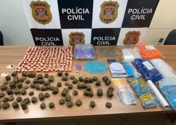 Mesa com drogas apreendidas pela DEIC Piracicaba, incluindo maconha, cocaína, dinheiro e materiais para embalo, em frente a painel da Polícia Civil de São Paulo.