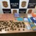 Mesa com drogas apreendidas pela DEIC Piracicaba, incluindo maconha, cocaína, dinheiro e materiais para embalo, em frente a painel da Polícia Civil de São Paulo.
