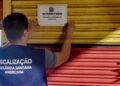 Agente da Vigilância Sanitária de Americana fixa aviso de interdição em porta metálica de estabelecimento durante operação de fiscalização noturna.