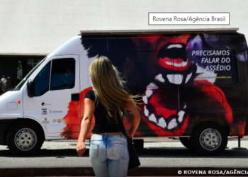 como denunciar assédio moral e sexual no trabalho #PraCegoVer mulher virada de costas com cabelo loiro, blusa preta e calça jeans, indo sentido a uma van com uma mulher desenhada e uma boca maior escrito "Precisamos falar do assédio