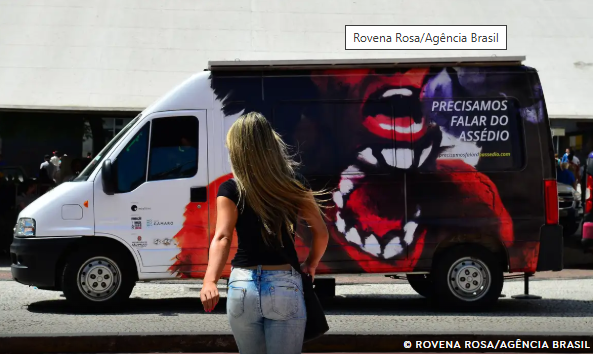 como denunciar assédio moral e sexual no trabalho #PraCegoVer mulher virada de costas com cabelo loiro, blusa preta e calça jeans, indo sentido a uma van com uma mulher desenhada e uma boca maior escrito "Precisamos falar do assédio