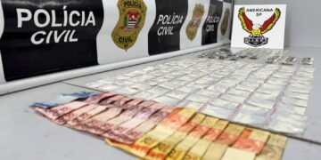 dise prende traficante no jardim aline #PraCegoVer: sobre uma superfície estão diversas porções de drogas embaladas organizadas em fileiras, além de notas de dinheiro em primeiro plano, com painel da Polícia Civil e identificação da DISE de Americana ao fundo