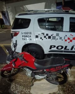 tráfico de drogas em Piracicaba #PraCegoVer: imagem mostra motocicleta vermelha estacionada ao lado de viatura da Força Tática da Polícia Militar durante a noite, após abordagem na Rodovia Luiz de Queiroz.