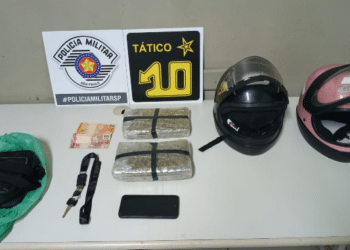 tráfico de drogas em Piracicaba #PraCegoVer: imagem mostra dois tijolos de maconha embalados sobre mesa ao lado de capacetes, celular e dinheiro, durante apresentação da ocorrência pela Polícia Militar.