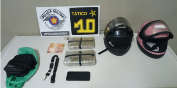 tráfico de drogas em Piracicaba #PraCegoVer: imagem mostra dois tijolos de maconha embalados sobre mesa ao lado de capacetes, celular e dinheiro, durante apresentação da ocorrência pela Polícia Militar.