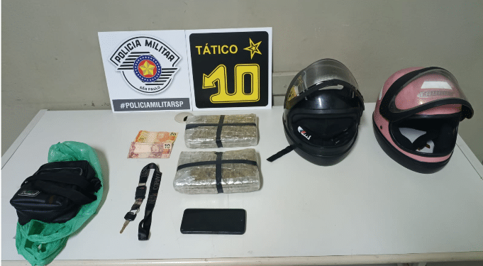 tráfico de drogas em Piracicaba #PraCegoVer: imagem mostra dois tijolos de maconha embalados sobre mesa ao lado de capacetes, celular e dinheiro, durante apresentação da ocorrência pela Polícia Militar.