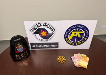 força tática prende traficante com cocaína #PraCegoVer: sobre uma mesa de madeira estão um distintivo da Força Tática, dois painéis com os logotipos da Polícia Militar e da Força Tática, ao centro munições organizadas em formato circular e ao lado notas de dinheiro apreendidas