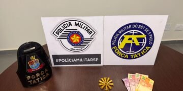 força tática prende traficante com cocaína #PraCegoVer: sobre uma mesa de madeira estão um distintivo da Força Tática, dois painéis com os logotipos da Polícia Militar e da Força Tática, ao centro munições organizadas em formato circular e ao lado notas de dinheiro apreendidas
