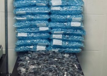 gcm apreende grande quantidade de drogas #PraCegoVer: sobre uma mesa estão diversos sacos plásticos com milhares de pinos azuis, além de embalagens com porções de drogas organizadas, ao fundo painel com símbolo do Apoio Tático da Guarda Civil Municipal