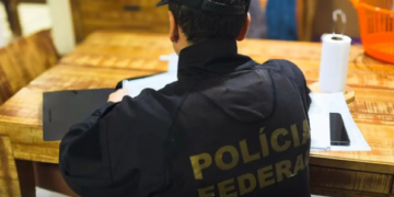 operação Bazaar contra corrupção policial realizada pelo GAECO e Polícia Federal #PraCegoVer imagem mostra agentes em operação policial cumprindo mandados, sentado em uma mesa de uma das residencias analisando documentos de interesse