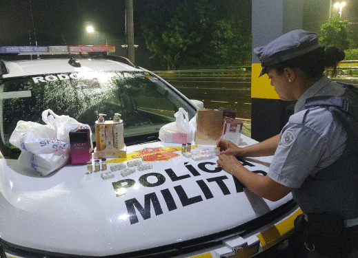contrabando de anabolizantes em Araçatuba #PraCegoVer: imagem mostra viatura da Polícia Militar Rodoviária parada às margens de rodovia durante a noite, com produtos apreendidos expostos após abordagem.