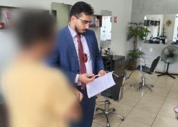 polícia civil investiga ameaças contra primeira-dama do df #PraCegoVer: policial civil em trajes formais segura documentos durante cumprimento de mandado em um salão comercial com cadeiras e espelhos ao fundo