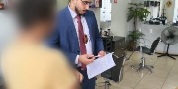 polícia civil investiga ameaças contra primeira-dama do df #PraCegoVer: policial civil em trajes formais segura documentos durante cumprimento de mandado em um salão comercial com cadeiras e espelhos ao fundo
