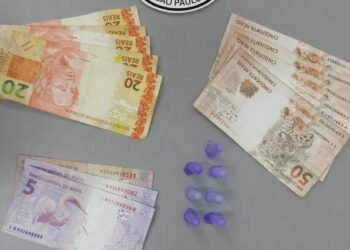 polícia militar prende traficante com cocaína #PraCegoVer: imagem mostra notas de dinheiro organizadas por valores, pequenos recipientes plásticos com droga ao centro e o emblema da Polícia Militar do Estado de São Paulo na parte superior