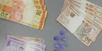 polícia militar prende traficante com cocaína #PraCegoVer: imagem mostra notas de dinheiro organizadas por valores, pequenos recipientes plásticos com droga ao centro e o emblema da Polícia Militar do Estado de São Paulo na parte superior