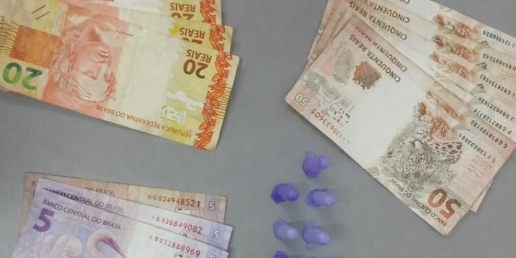 polícia militar prende traficante com cocaína #PraCegoVer: imagem mostra notas de dinheiro organizadas por valores, pequenos recipientes plásticos com droga ao centro e o emblema da Polícia Militar do Estado de São Paulo na parte superior