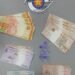 polícia militar prende traficante com cocaína #PraCegoVer: imagem mostra notas de dinheiro organizadas por valores, pequenos recipientes plásticos com droga ao centro e o emblema da Polícia Militar do Estado de São Paulo na parte superior