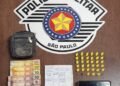Apreensão de tráfico de drogas realizada pela Polícia Militar em Leme #PraCegoVer Na imagem aparecem 33 eppendorfs amarelos com cocaína organizados sobre uma mesa, dinheiro em notas de real, um celular, uma pequena bolsa e anotações do tráfico ao fundo com o brasão da Polícia Militar de São Paulo.