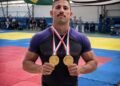policial militar conquista ouro duplo no jiu jitsu apmbb 2026 #PraCegoVer: policial militar posa em tatame segurando duas medalhas de ouro no peito, com bandeiras do Brasil e do Estado de São Paulo ao fundo, durante campeonato de jiu-jítsu.