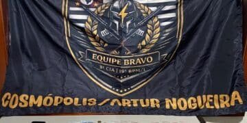 PM prende homem por trafico de drogas #PraCegoVer imagem mostra drogas, dinheiro e um celular apreendidos sobre uma mesa, com bandeira da Polícia Militar ao fundo
