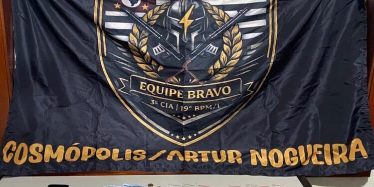 PM prende homem por trafico de drogas #PraCegoVer imagem mostra drogas, dinheiro e um celular apreendidos sobre uma mesa, com bandeira da Polícia Militar ao fundo
