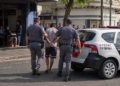 PM prende homem por coação no curso do processo #PraCegoVer dois policiais militares escoltam um homem algemado ao lado de uma viatura da Polícia Militar em frente a um bar, durante ocorrência policial em via urbana