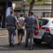 PM prende homem por coação no curso do processo #PraCegoVer dois policiais militares escoltam um homem algemado ao lado de uma viatura da Polícia Militar em frente a um bar, durante ocorrência policial em via urbana