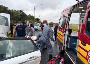 mulher encontrada com vida em porta-malas #PraCegoVer agentes da Guarda Municipal, policiais e bombeiros atendem uma vítima ao lado de um carro branco e de uma ambulância do Corpo de Bombeiros em uma via molhada