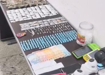 PM prende casal por tráfico de drogas em adega #PraCegoVer imagem mostra uma mesa com várias porções de drogas embaladas, microtubos, dinheiro, máquinas de cartão e câmeras de vigilância apreendidos pela Polícia Militar