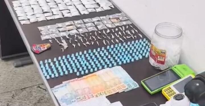 PM prende casal por tráfico de drogas em adega #PraCegoVer imagem mostra uma mesa com várias porções de drogas embaladas, microtubos, dinheiro, máquinas de cartão e câmeras de vigilância apreendidos pela Polícia Militar