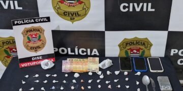 operação Open Doors III contra o tráfico de drogas #PraCegoVer: imagem mostra materiais apreendidos sobre uma mesa, com porções de drogas embaladas, dinheiro em espécie, três celulares, balança de precisão, colher, faca e isqueiros, diante de um painel da Polícia Civil de São Paulo e placa da DISE de Votuporanga.