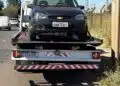 GCM prende homem após perseguição em Americana #PraCegoVer carro preto sobre caminhão-guincho em avenida, com postes, fios elétricos, céu azul e área de mato ao lado da via