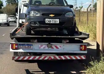 GCM prende homem após perseguição em Americana #PraCegoVer carro preto sobre caminhão-guincho em avenida, com postes, fios elétricos, céu azul e área de mato ao lado da via