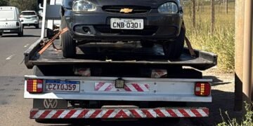 GCM prende homem após perseguição em Americana #PraCegoVer carro preto sobre caminhão-guincho em avenida, com postes, fios elétricos, céu azul e área de mato ao lado da via
