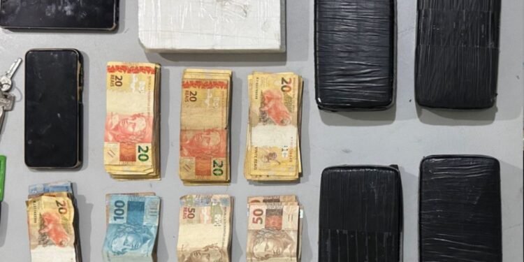 **Text Alt:** Força Tática apreende mais de 5 kg de drogas em Catanduva #PraCegoVer: mesa com tijolos de drogas embalados, dinheiro em espécie, celulares e chave de veículo apreendidos pela Polícia Militar durante ocorrência de tráfico de drogas