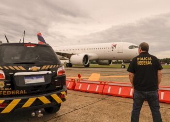PF prende três suspeitos durante fiscalização migratória no Aeroporto de Guarulhos #PraCegoVer: imagem mostra uma viatura da Polícia Federal estacionada na pista do Aeroporto Internacional de Guarulhos enquanto um agente federal observa uma aeronave comercial ao fundo durante operação de fiscalização.