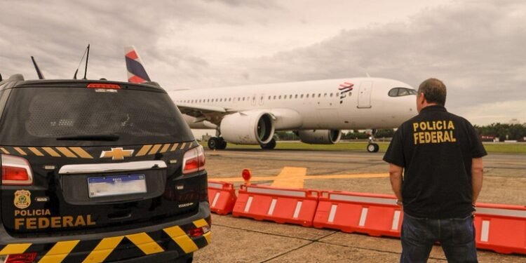 PF prende três suspeitos durante fiscalização migratória no Aeroporto de Guarulhos #PraCegoVer: imagem mostra uma viatura da Polícia Federal estacionada na pista do Aeroporto Internacional de Guarulhos enquanto um agente federal observa uma aeronave comercial ao fundo durante operação de fiscalização.