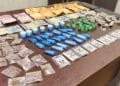 tráfico de drogas no Vida Nova #PraCegoVer: imagem mostra uma mesa com porções de drogas embaladas, dinheiro em notas e moedas, além de embalagens separadas para apresentação da ocorrência policial.