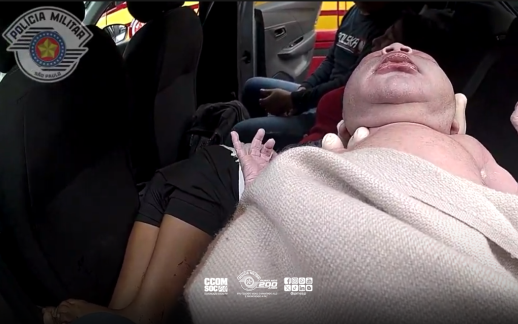 mãe boliviana dá à luz em carro de aplicativo. #PraCegoVer policial segurando recém-nascido
