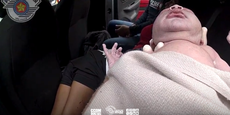 mãe boliviana dá à luz em carro de aplicativo. #PraCegoVer policial segurando recém-nascido